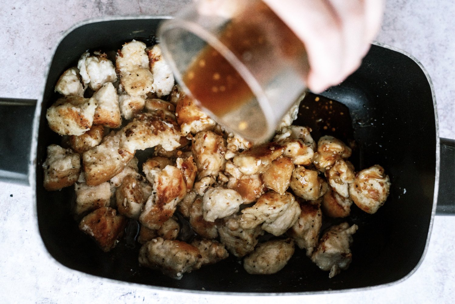 pouring sauce over browned chicken in slow cooker