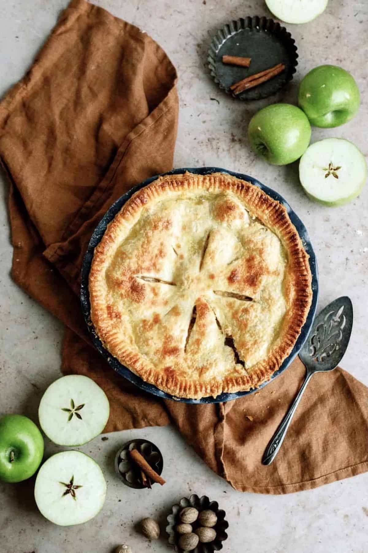 Top view of a fresh baked Classic Apple Pie with other sliced apples around the pie.