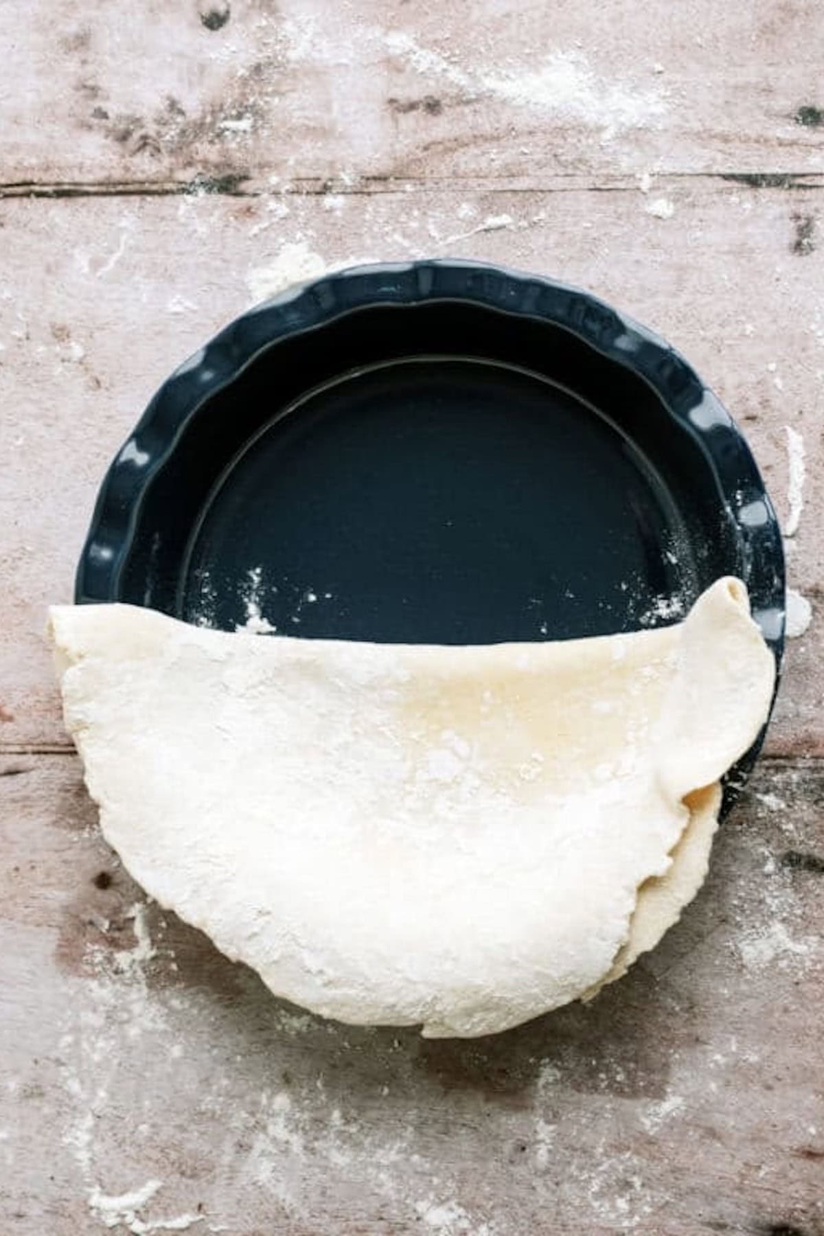 A pie plate half covered by a folded over pie crust.