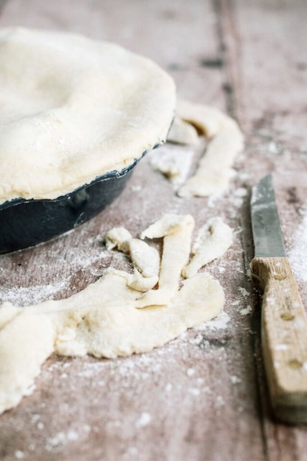 Unbaked pie with trimmed pastry edges on a floured surface next to a knife and scraps of dough.