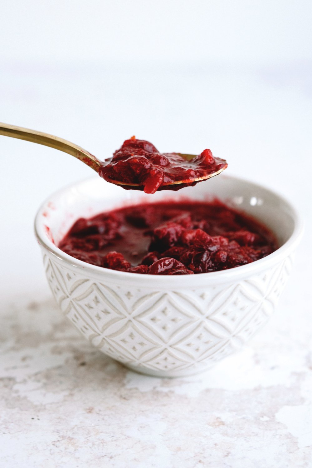 Cranberry sauce in a white bowl being scooped out with a spoon