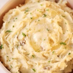 A bowl of mashed potatoes topped with melted butter and sprinkled with chopped parsley.