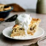 Slice of Apple Pie on a plate topped with whip cream with a fork on the side.