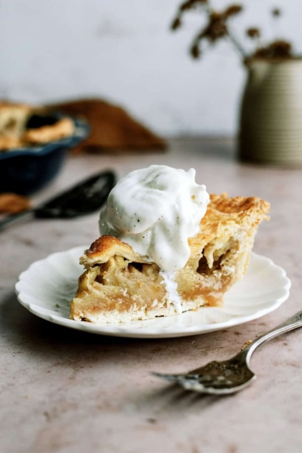 Slice of Apple Pie on a plate topped with whip cream with a fork on the side.