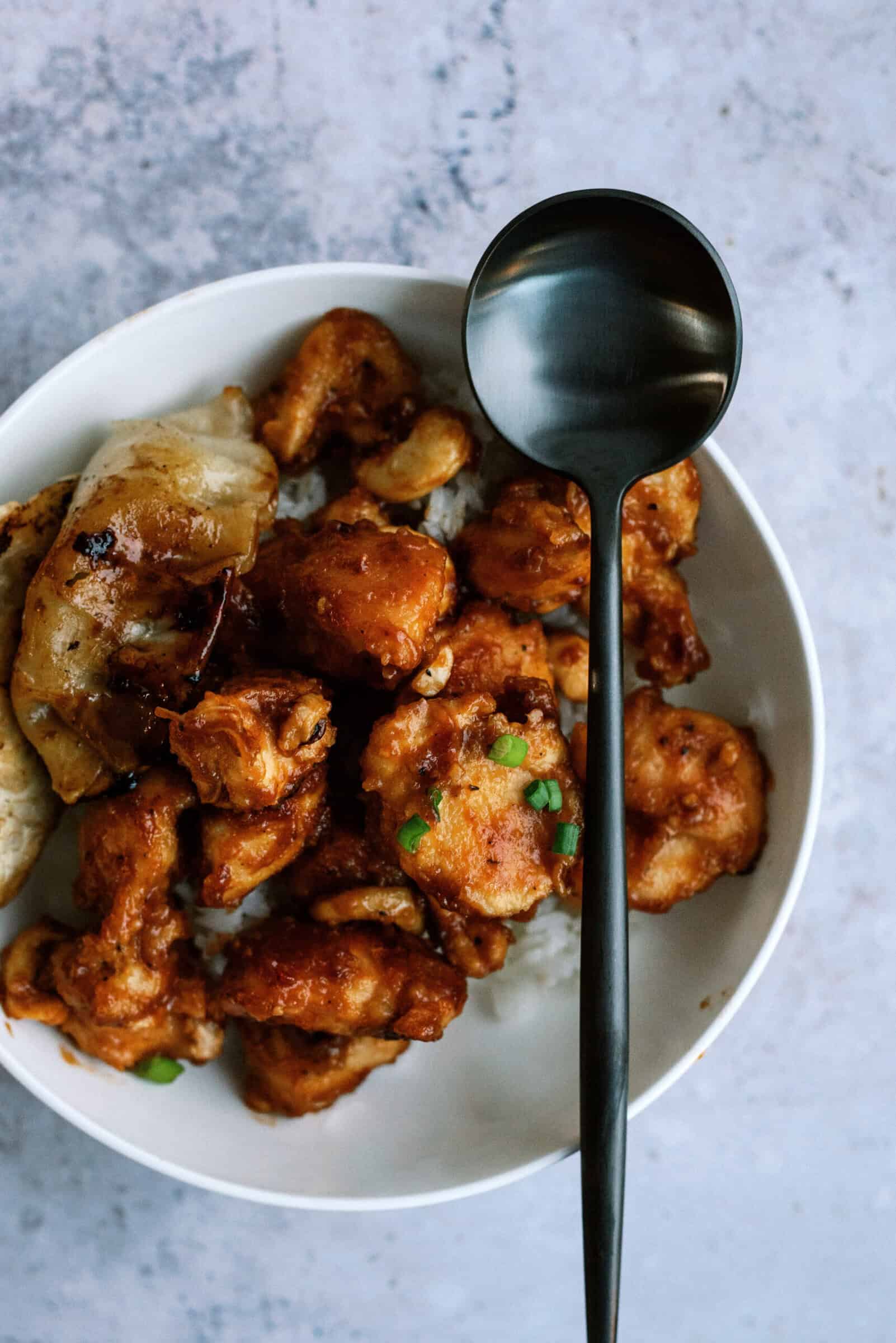 cashew chicken on a plate with rice and a large serving spoon