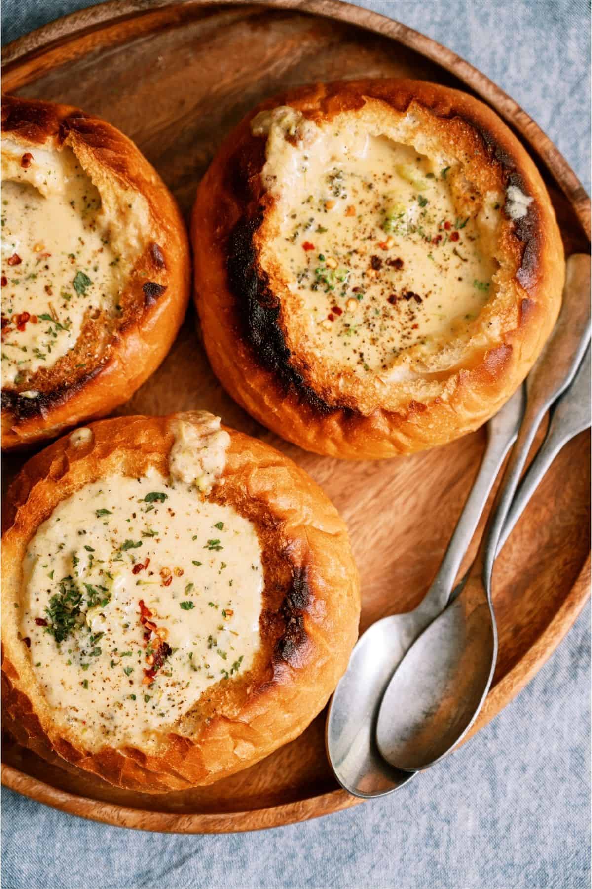 3 bread bowls on a serving platter filled with Slow Cooker Broccoli Cheddar Soup.