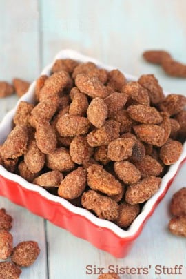 A square red dish filled with sugar-coated almonds, with a few more almonds scattered around the base.