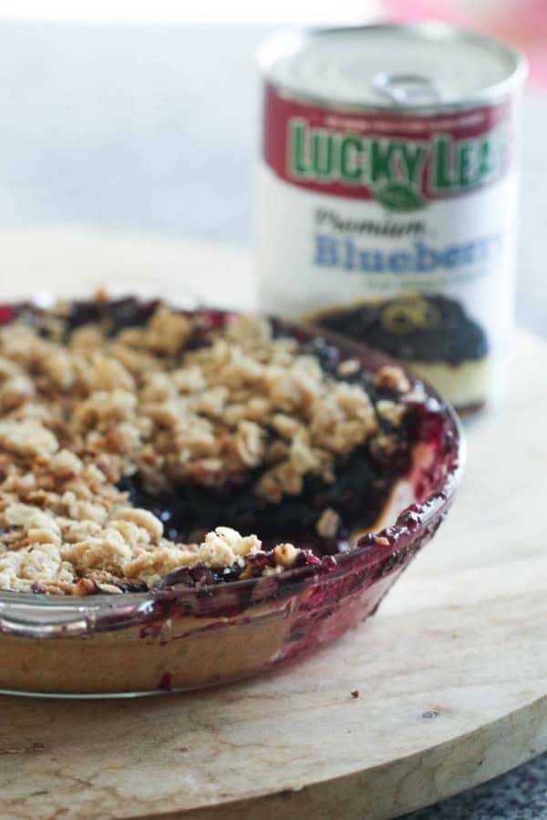 A blueberry pie in a glass pie plate missing a piece of pie. A can of Lucky Leaf Blueberry Pie Filling in the background.