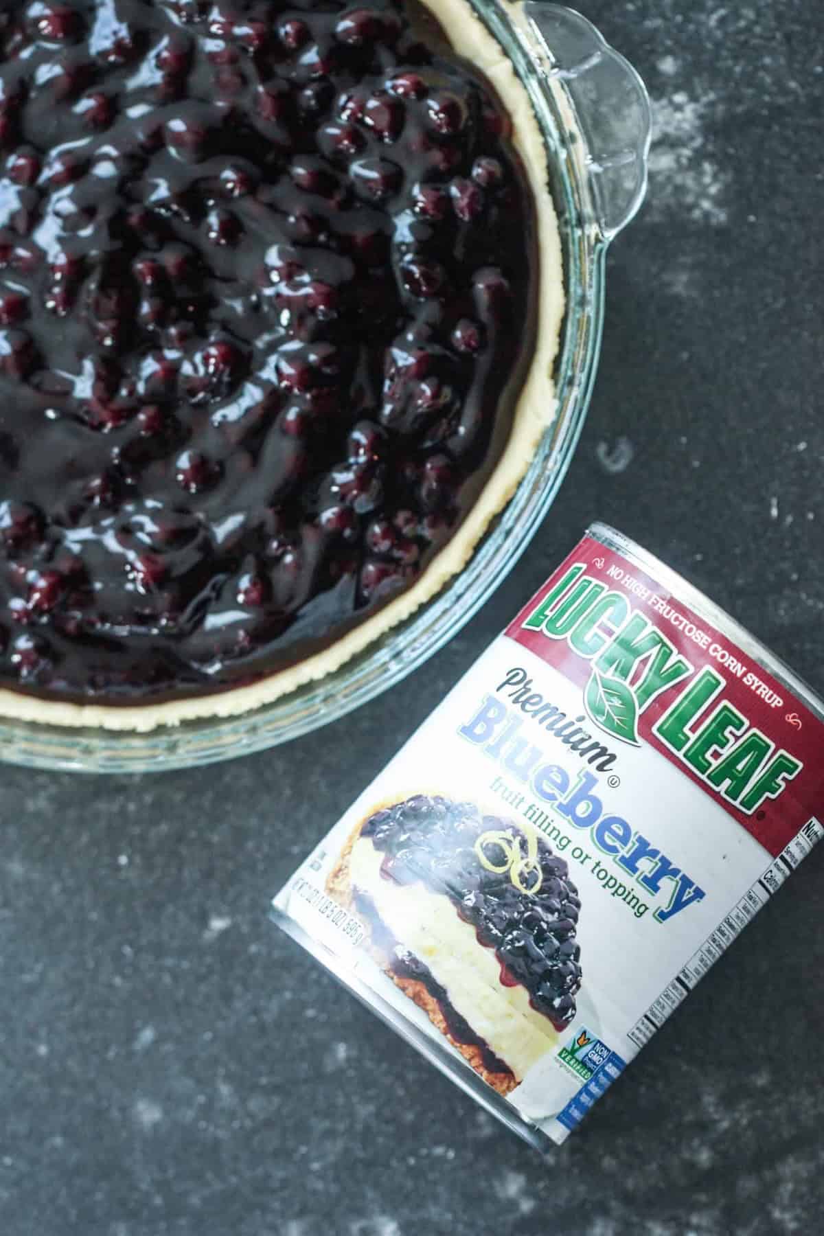 A blueberry pie in a glass pie plate with a can of blueberry pie filling next to the pie plate.