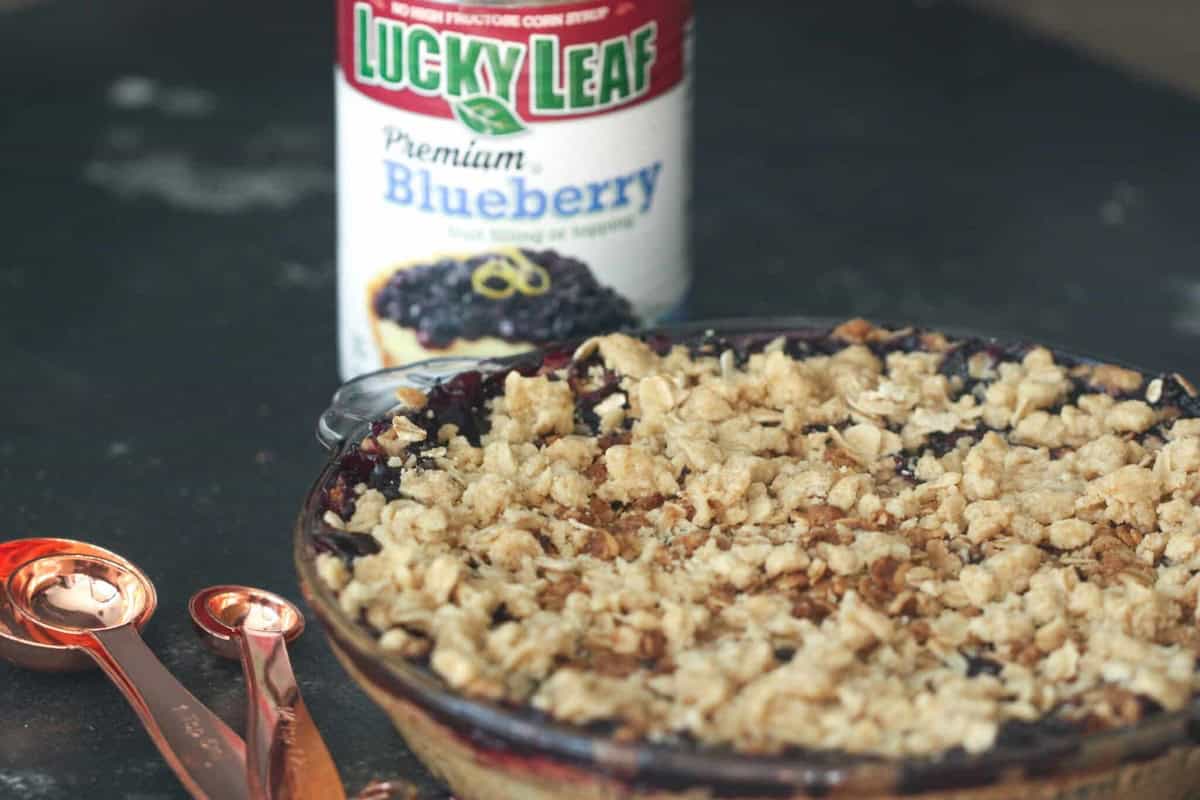 Baked Blueberry Crumble Pie with a can of blueberry pie filling in the background and a set of measuring spoons off to the side.