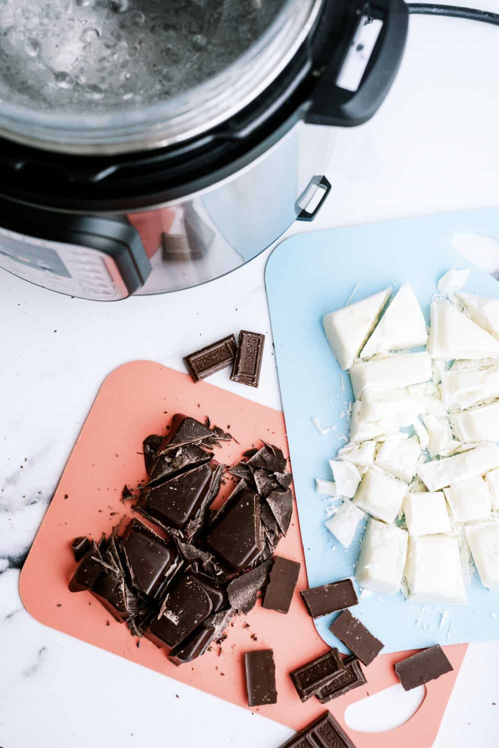 2 cutting boards with chopped white and milk chocolate. An instant pot with a glass bowl sitting on top.