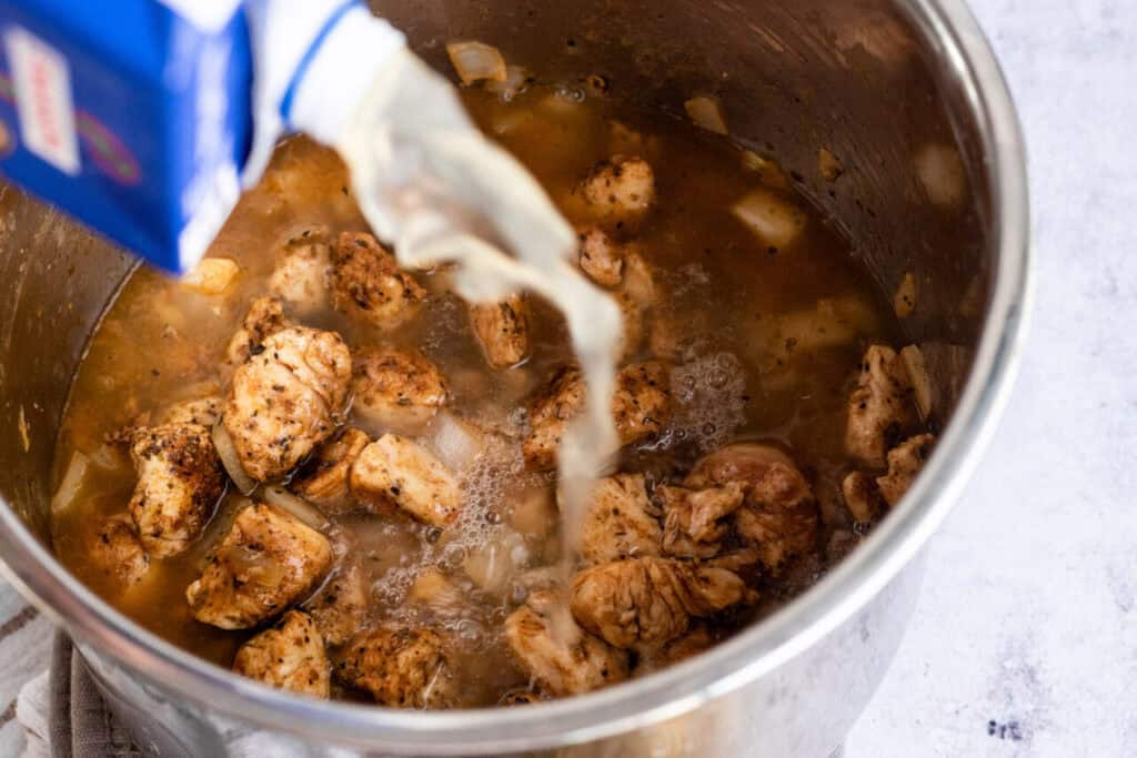 Adding chicken broth to chicken in the Instant Pot.
