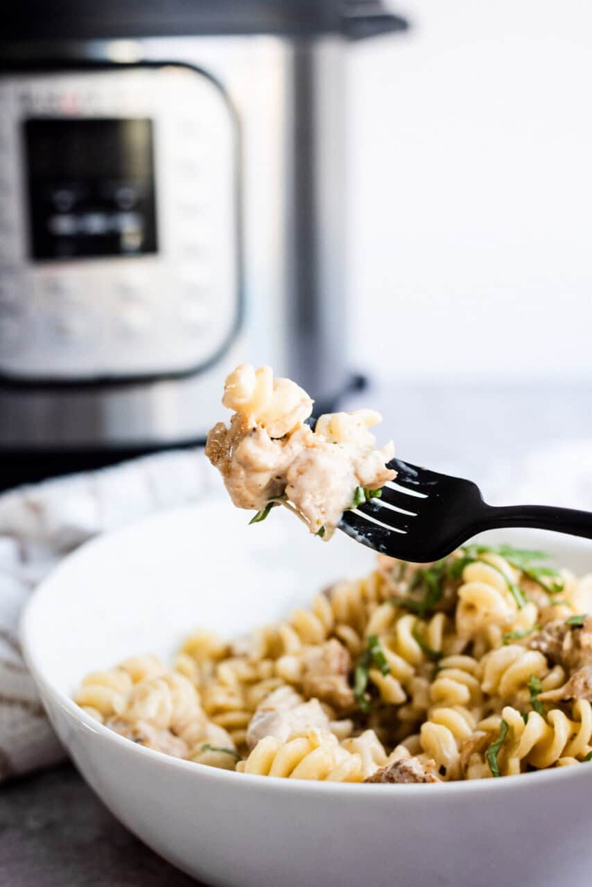 finished instant pot cheesy chicken and pasta, plated and a fork with a bite on it