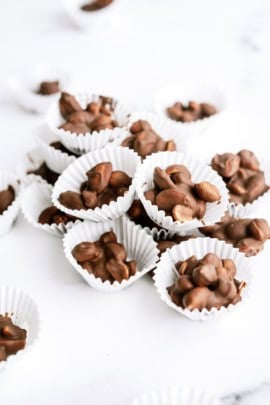 Paper cups filled with clusters of chocolate-covered almonds placed on a white surface.