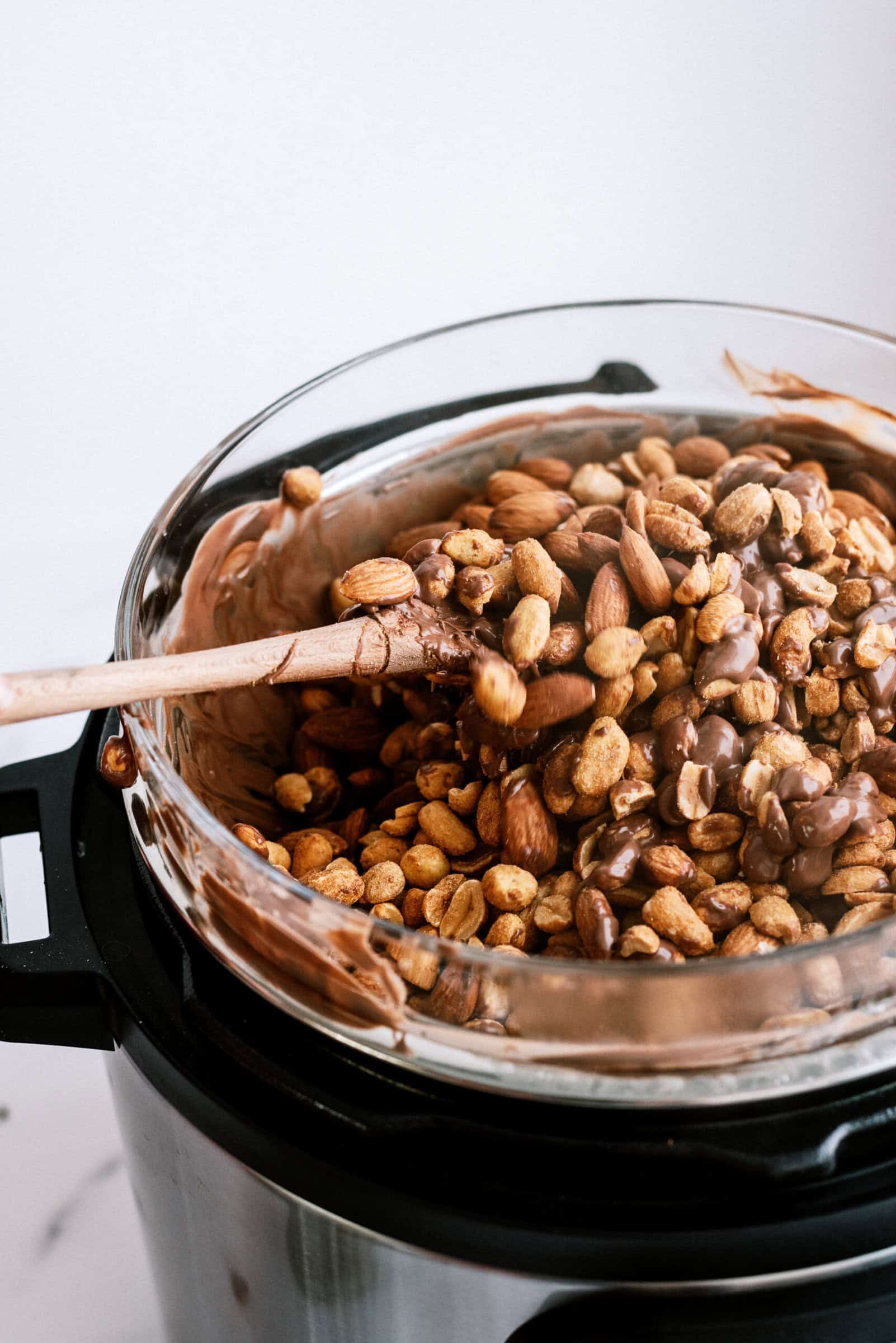 A wooden spoon stirring in nuts to the melted chocolate in glass bowl on top of the Instant Pot.