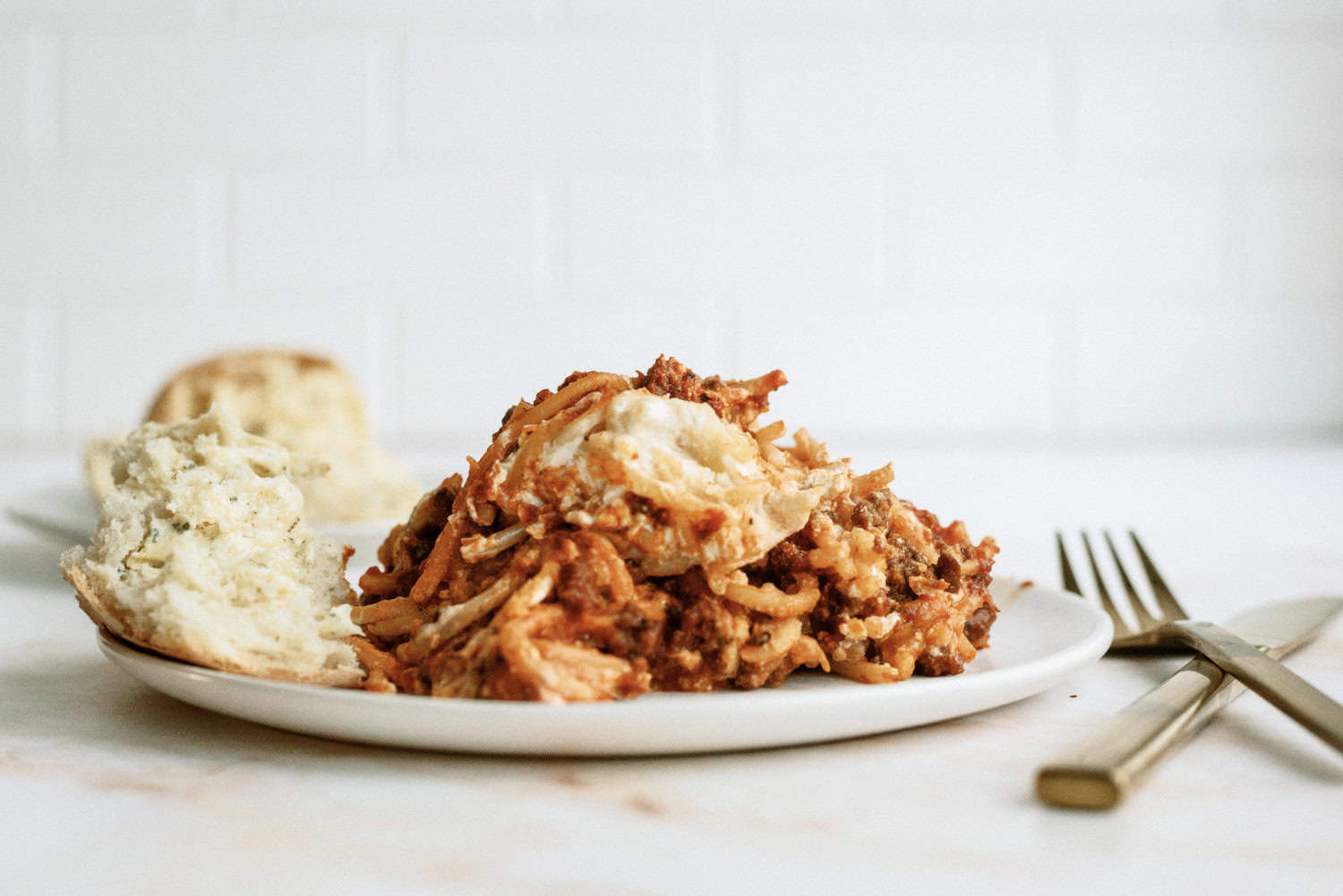 spaghetti casserole on a plate with rolls