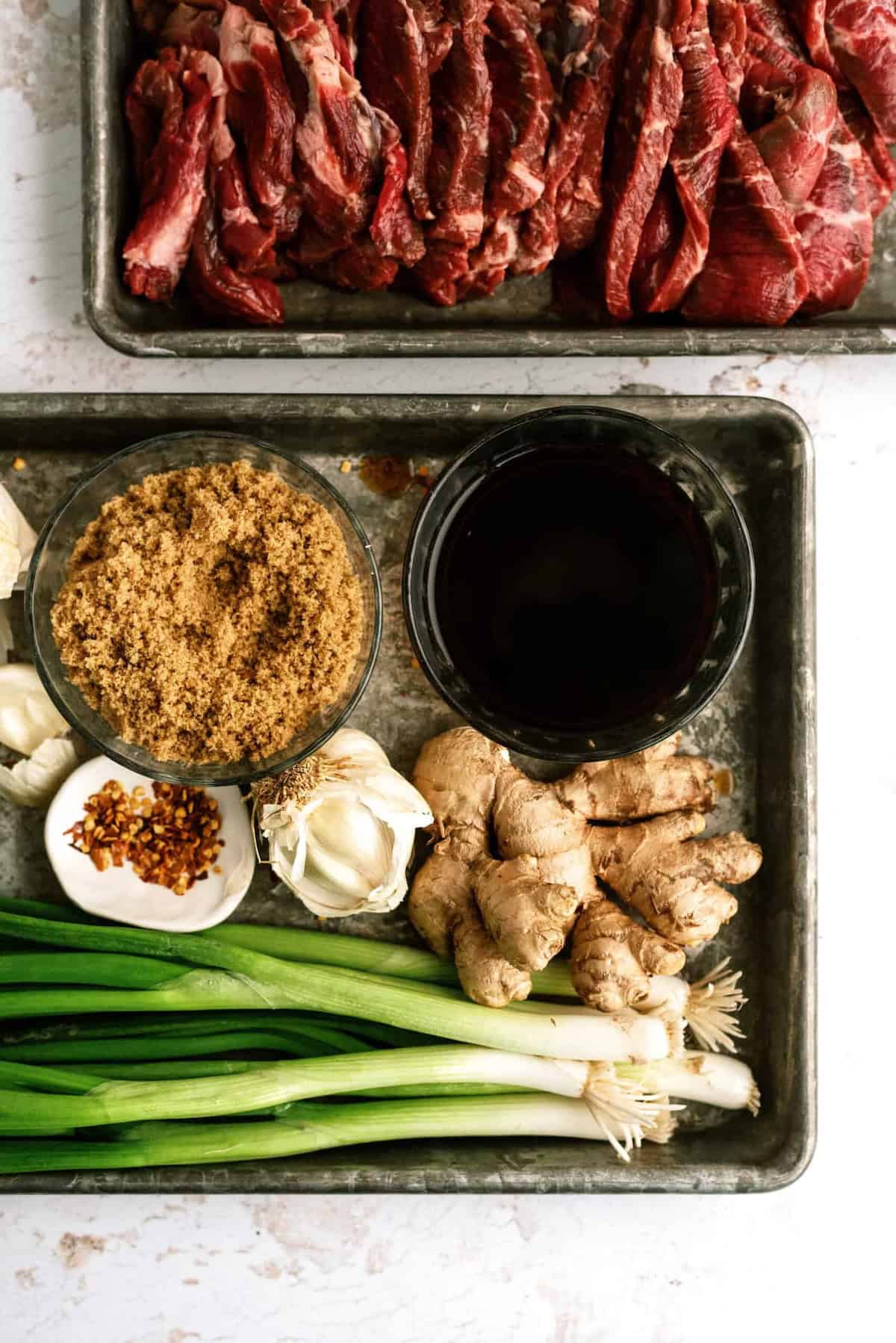 Raw beef, green onions, garlic, ginger, soy sauce, and brown sugar on a tray.