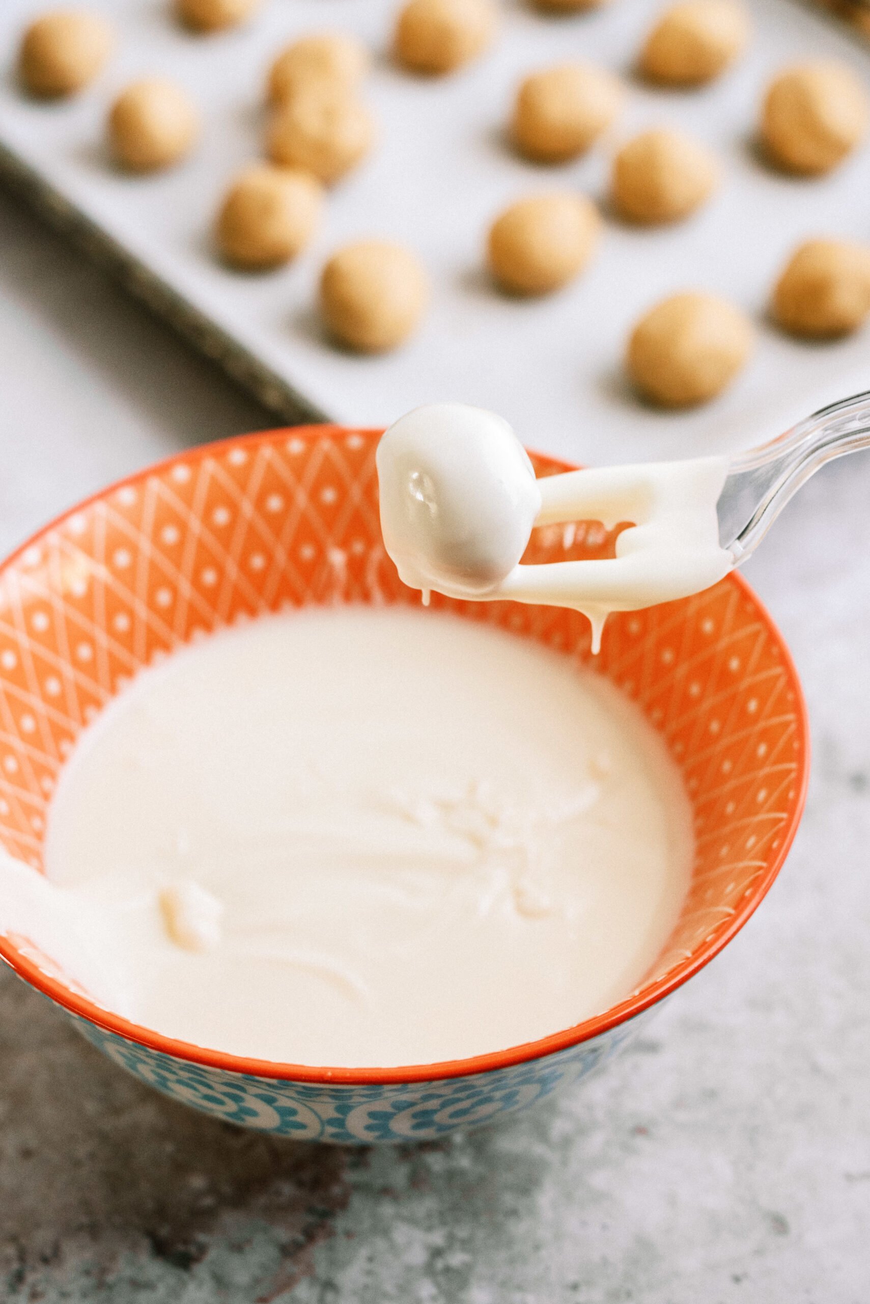 peanut butter ball coming out of the bowl of melted white chocolate