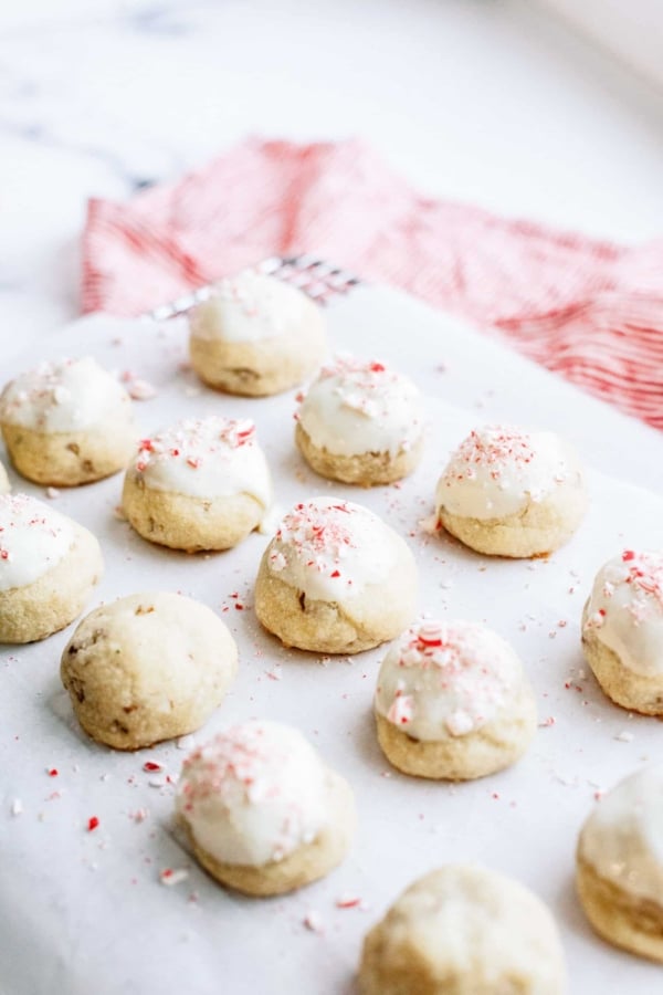 A dozen frosted cookies with white icing and red sprinkles arranged on a white surface with a red and white cloth in the background.