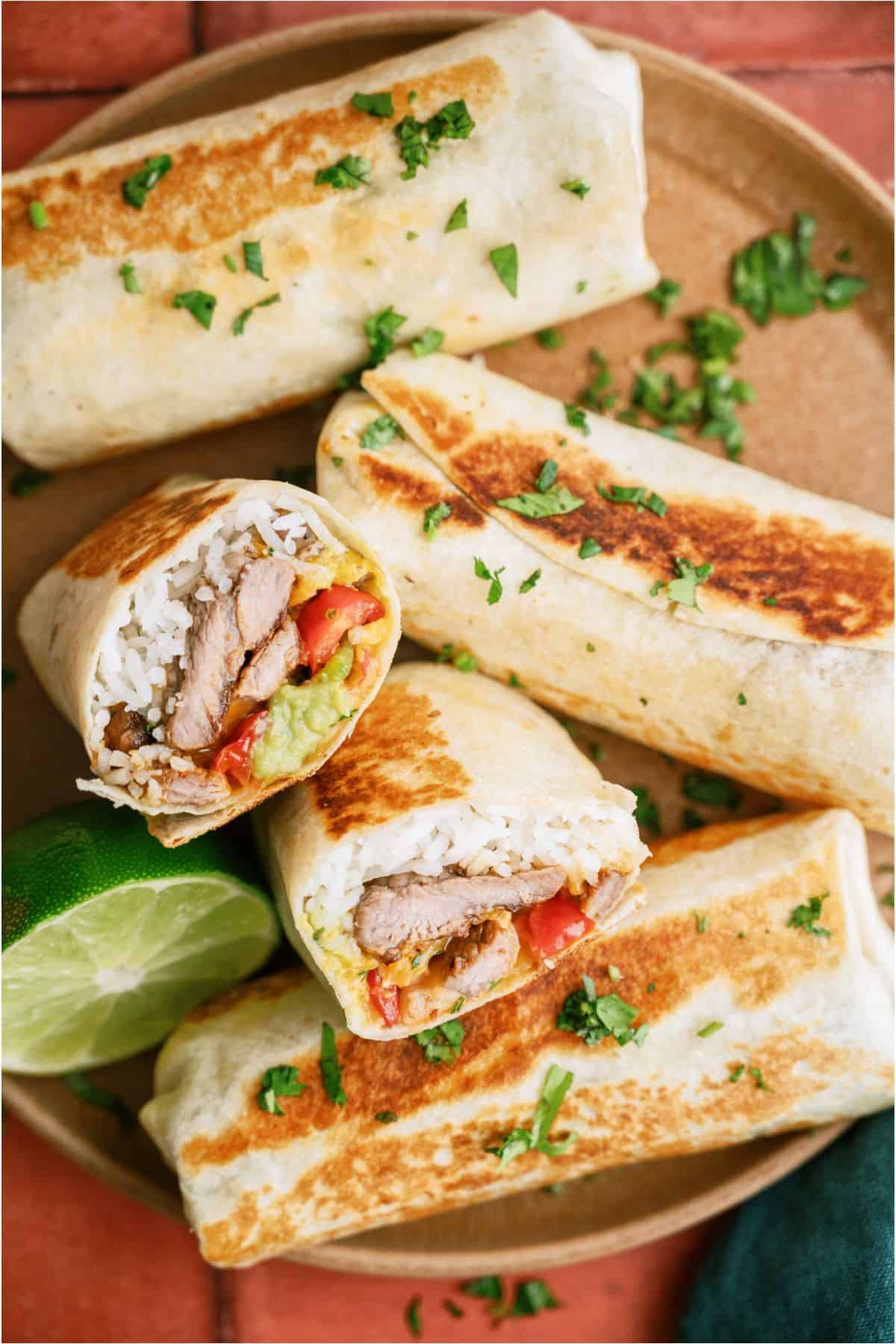 4 Crispy Steak Burritos on a plate with one cut in half to show the inside of the burrito.