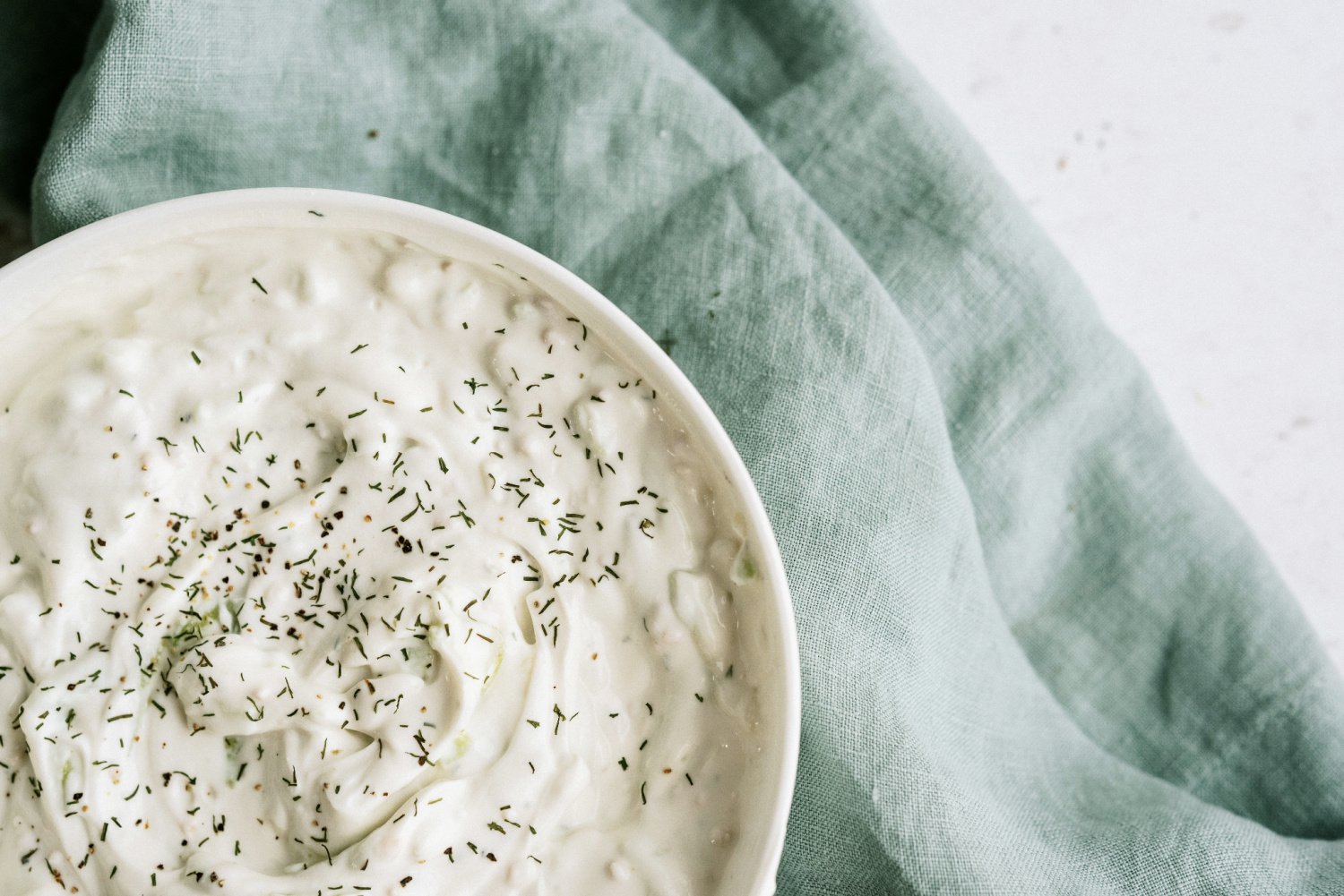 homemade tzatziki sauce in a white bowl with dill weed sprinkled on top