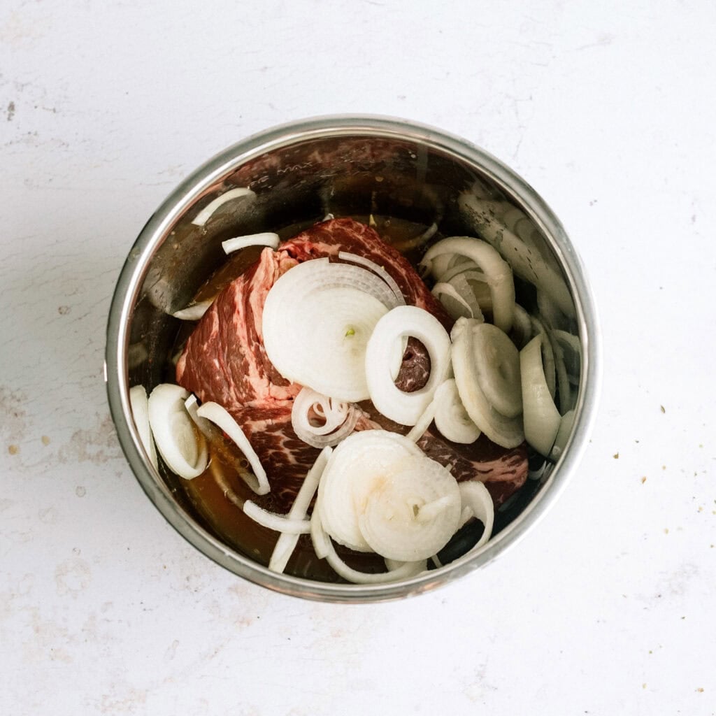 Beef roast in the instant pot topped with sliced onions.