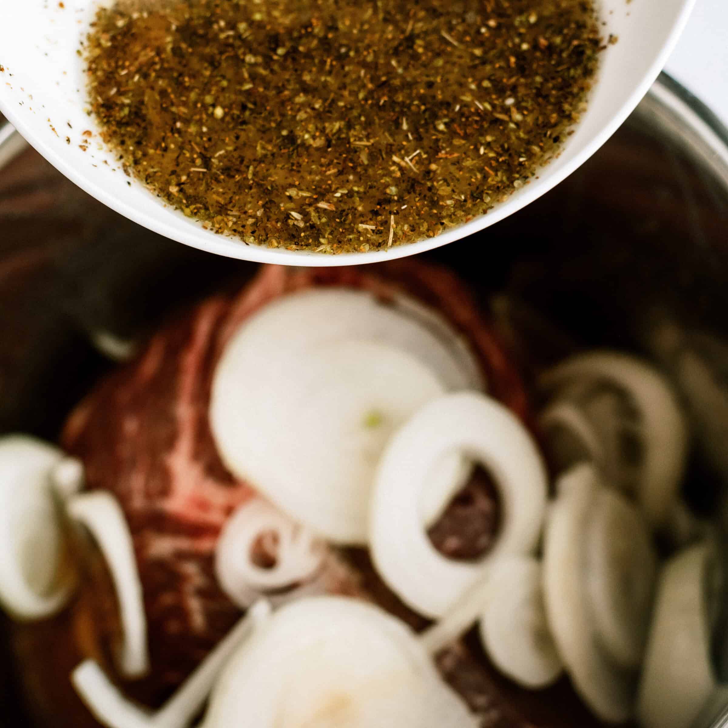 beef broth and seasonings poured on top of beef and onions in instant pot