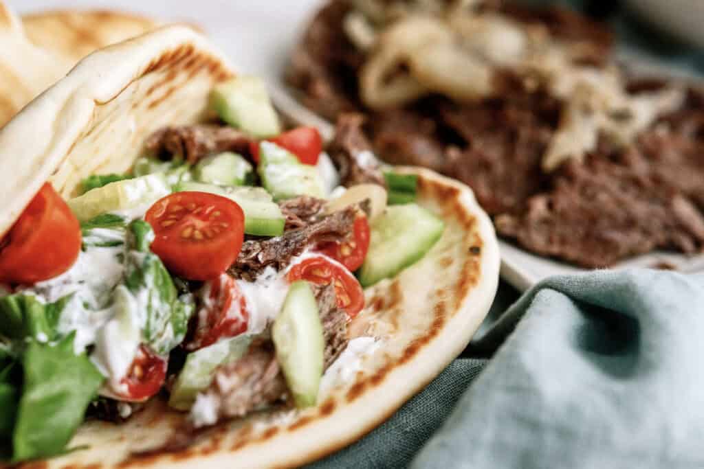 Instant Pot Beef Gyros on a plate with a plate of sliced beef and onions in the background.