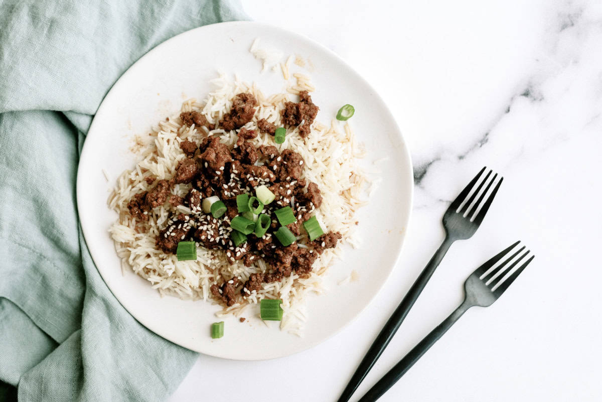 korean ground beef and rice topped with green onions and sesame seeds on a white plate