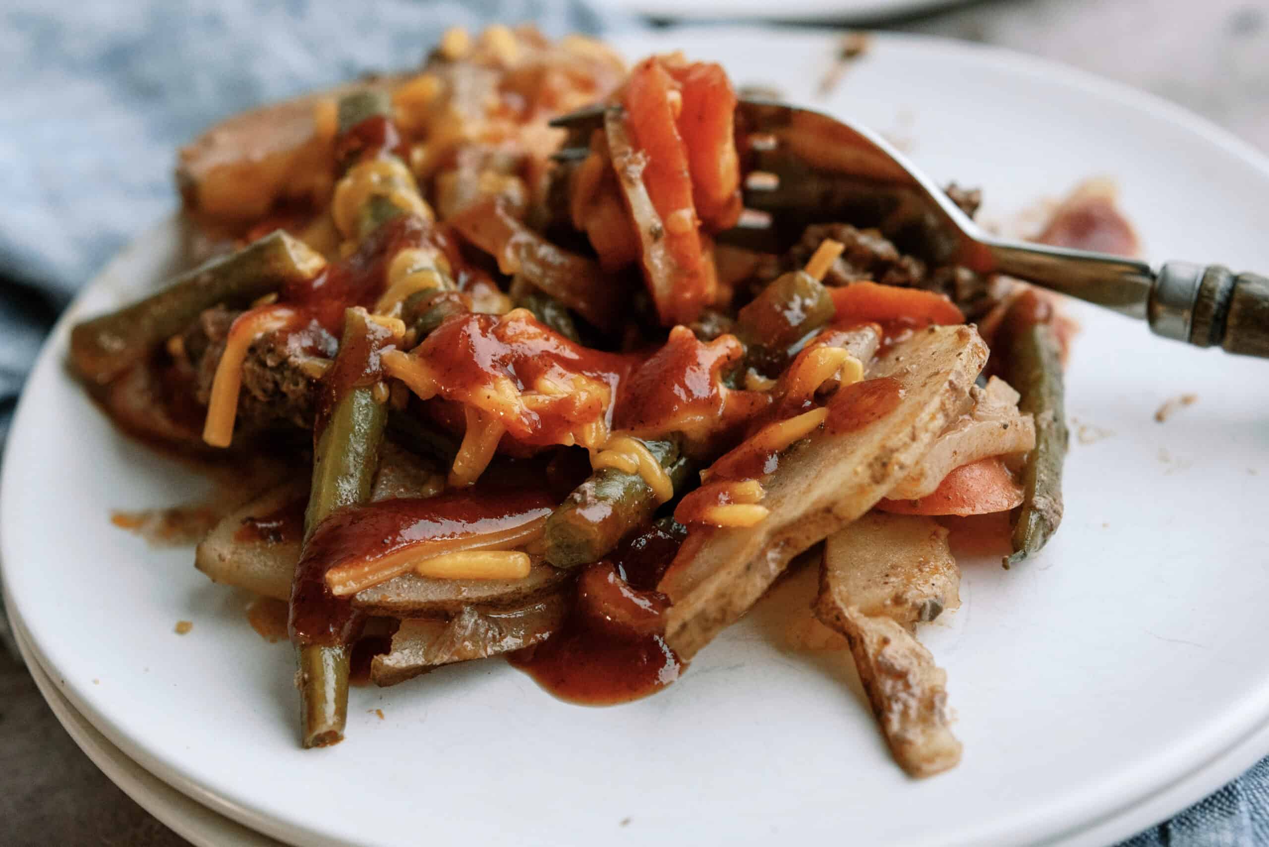 slow cooker hobo dinner on a white plate with bbq sauce on top