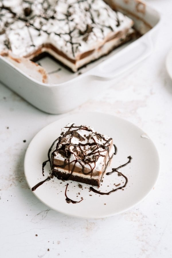 A slice of Layered Brownie Pudding Dessert on a plate with the remaining dessert in the background.