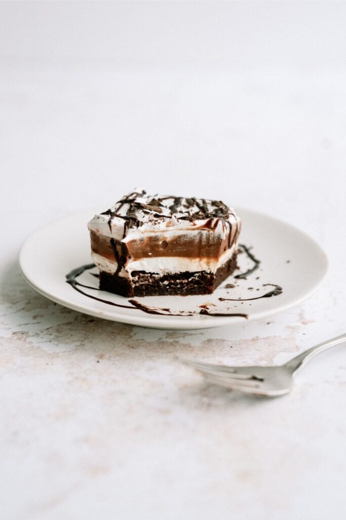 A slice of Layered Brownie Pudding Dessert on a plate with a bite missing to show the layeres.
