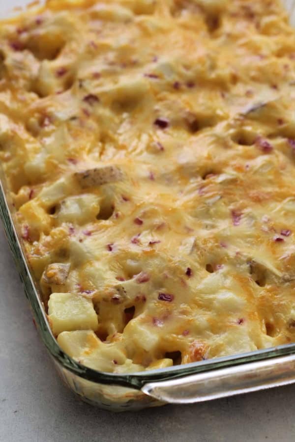 A glass baking dish filled with a baked casserole featuring melted cheese and visible chunks of potatoes.