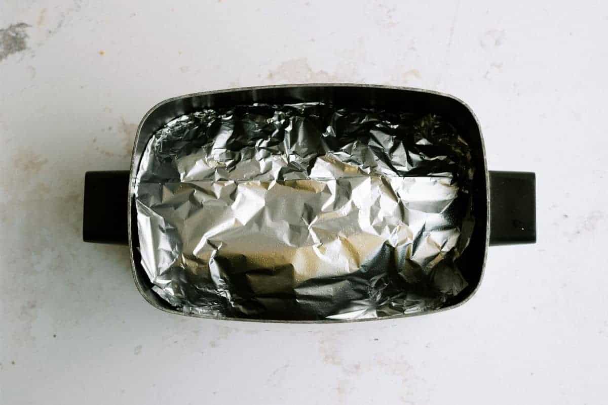 A rectangular baking dish lined with crumpled aluminum foil, viewed from above on a light-colored surface.