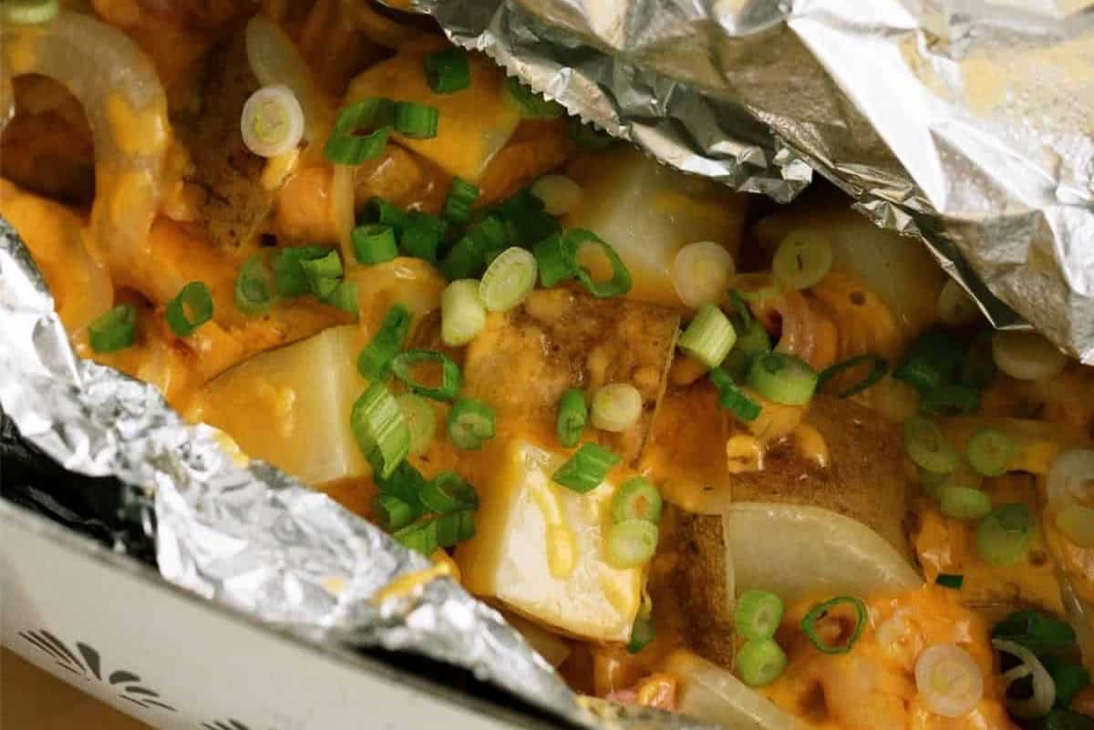 Chopped potatoes topped with melted cheese and sliced green onions, served in a foil packet.