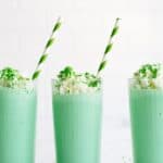 3 Copycat McDonald’s Shamrock Shakes in glasses topped with whip cream and sprinkles with a green striped straw in each glass.