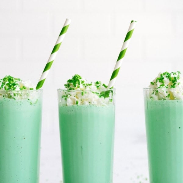 3 Copycat McDonald’s Shamrock Shakes in glasses topped with whip cream and sprinkles with a green striped straw in each glass.