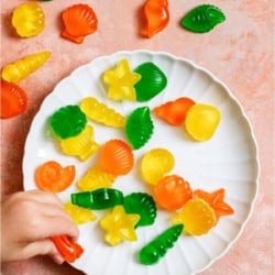 A plate of Homemade Jello Fruit Snacks with a little hand grabbing one.