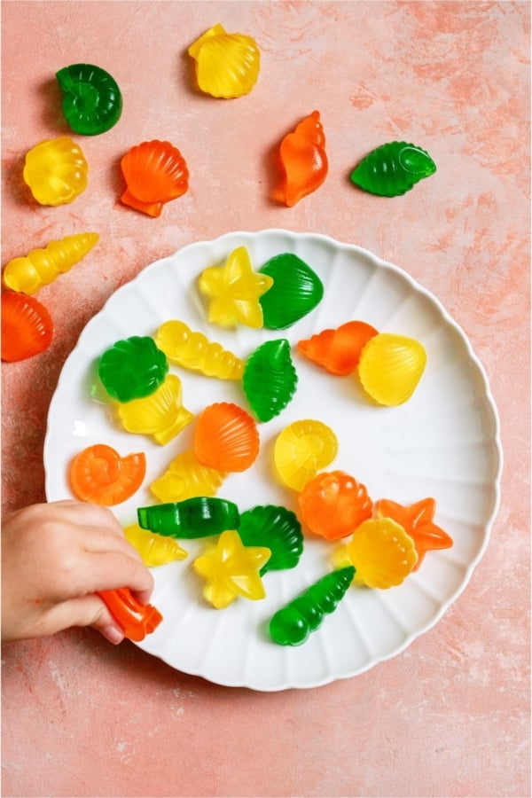 A plate of Homemade Jello Fruit Snacks with a little hand grabbing one.