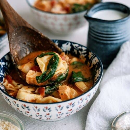 A wooden spoon lifting a bite of Instant Pot Creamy Tortellini Soup from a bowl.