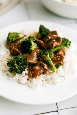 A white plate with slow cooker beef and broccoli served over white rice.