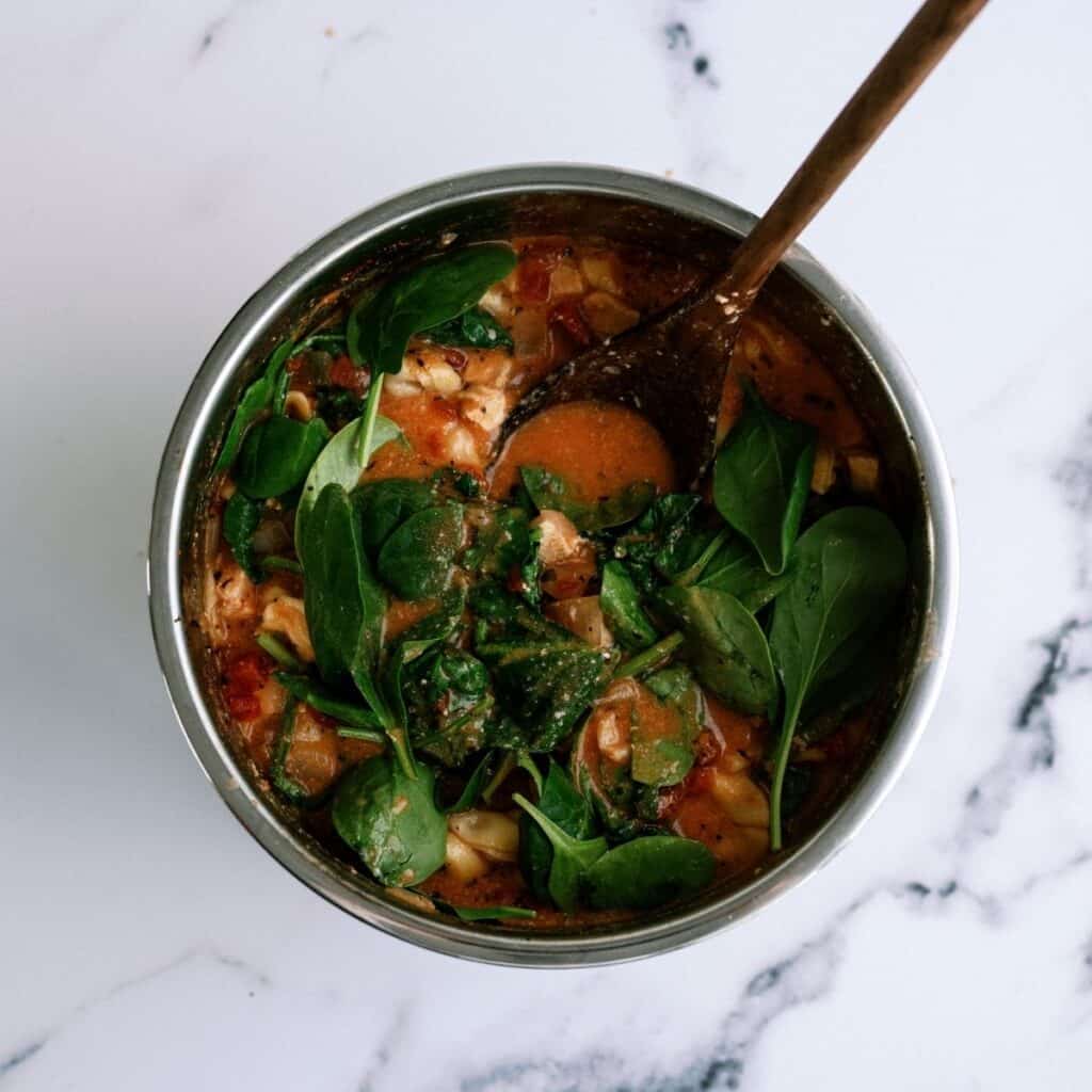 Fresh spinach added to instant pot, being stirred in by a wooden spoon.
