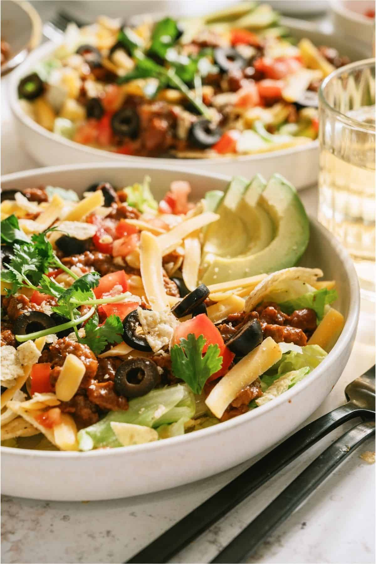Two bowls of taco salad with toppings.