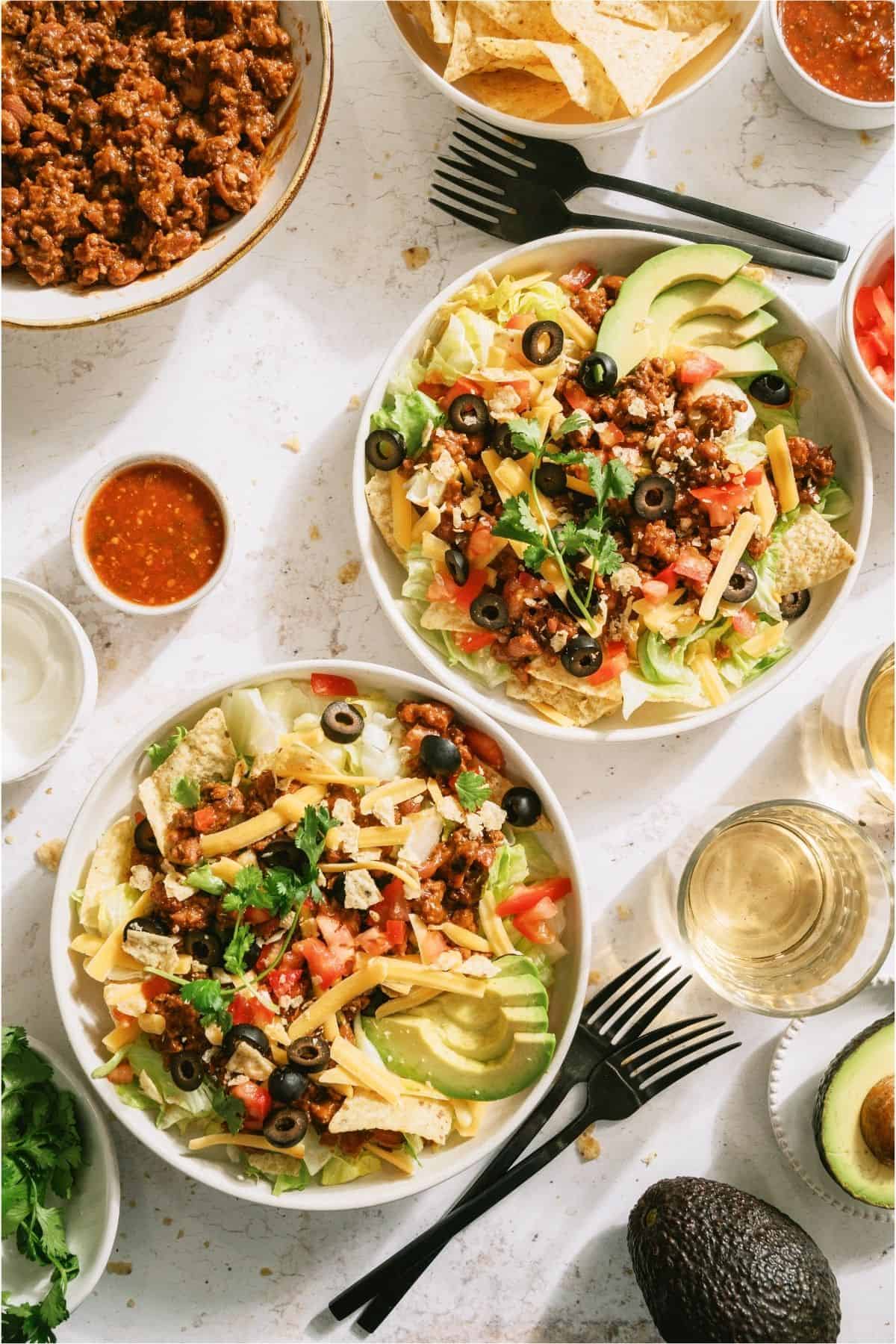 Two bowls of taco salad with toppings.