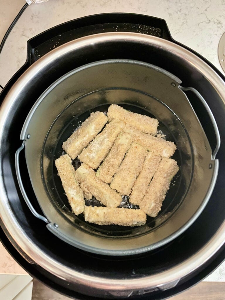 breaded zucchini in the bottom of an air fryer pan