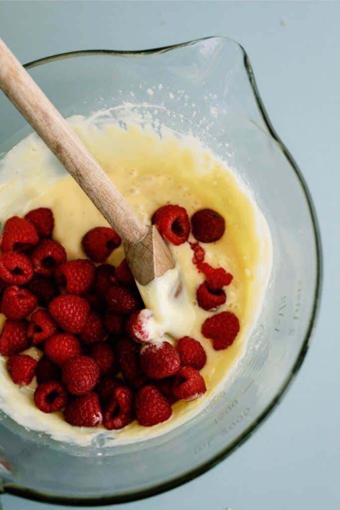 Lemon Batter in a bowl mixing in fresh raspberries with a wooden spoon.