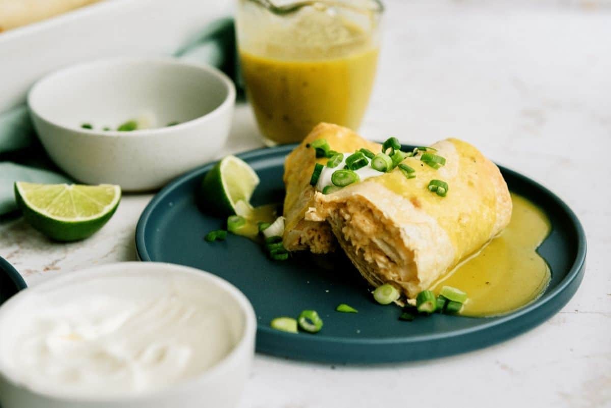 Baked Chicken Chimichanga cut in half served on a plate with lime wedges and sour cream on the side