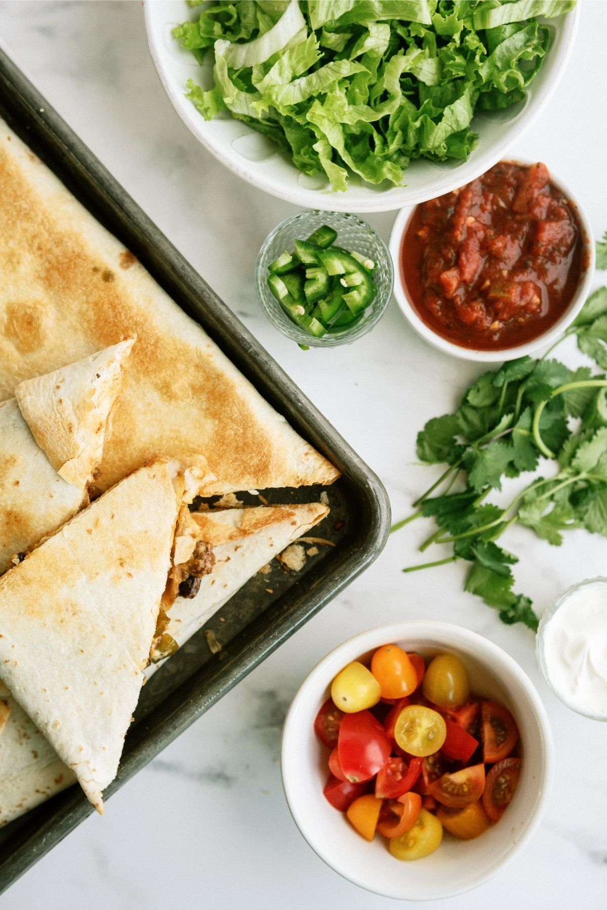 Baked Sheet Pan Ground Beef Quesadillas Recipe surrounded by toppings in white bowls