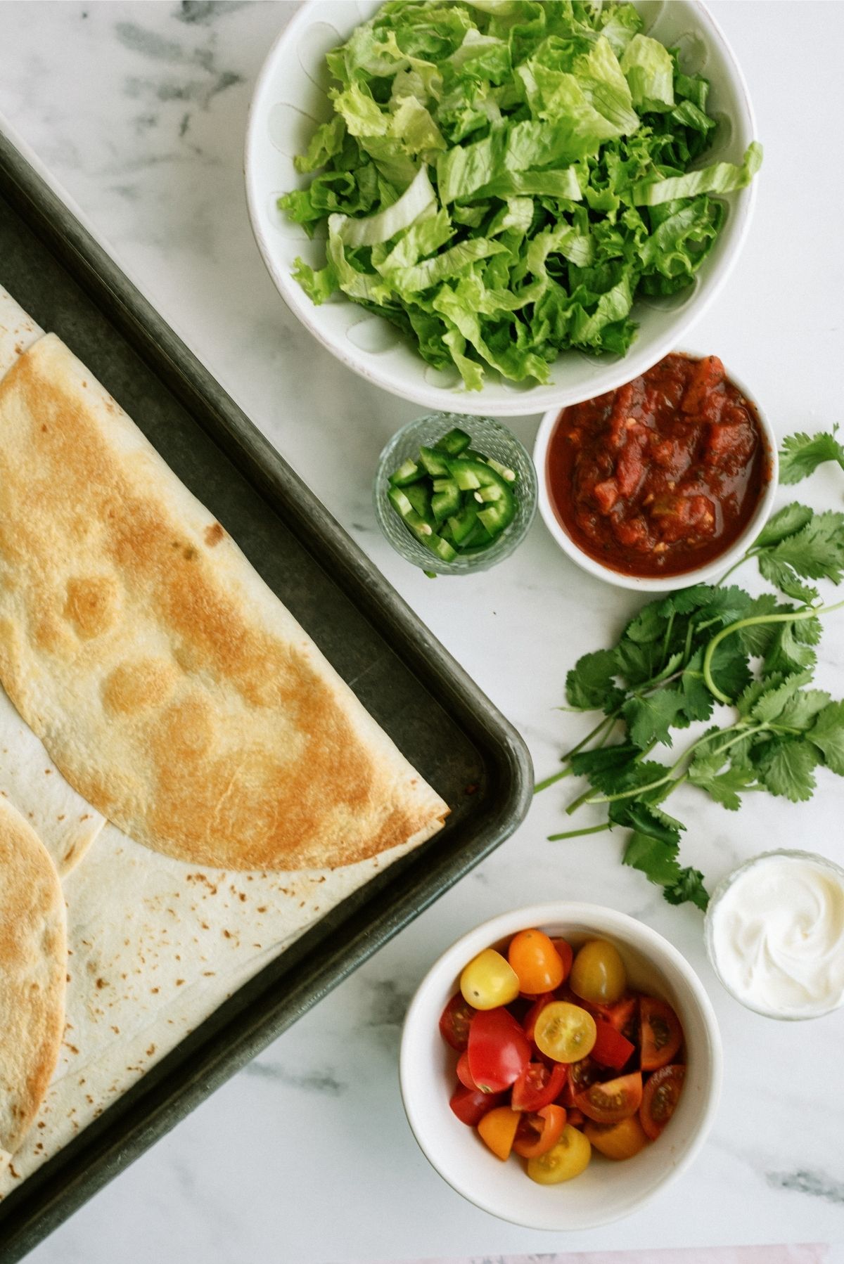 Baked Sheet Pan Ground Beef Quesadillas surrounded by toppings that are in white bowls