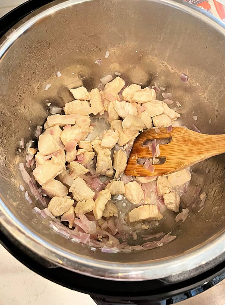 Chicken and Onion sauteed in the Instant Pot with a wooden spoon.
